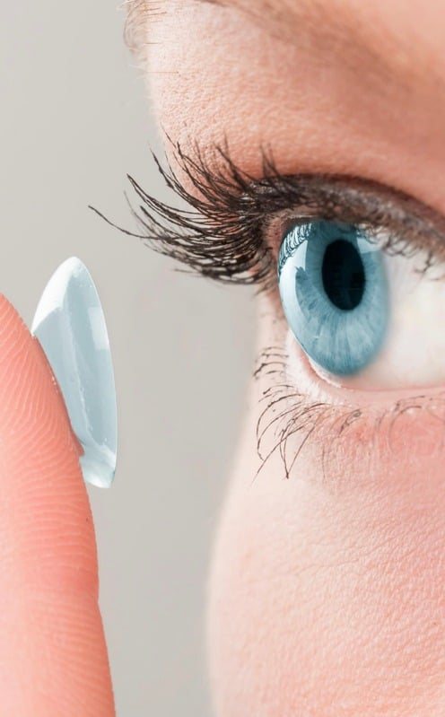 Lente de contacto sobre un dedo, frente a un ojo azul